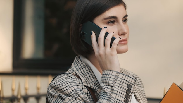 Nahaufnahme einer schönen Immobilienmaklerin, die auf dem Smartphone auf wartende Kunden auf der Straße spricht Moderne Geschäftsfrau, die im Freien arbeitet