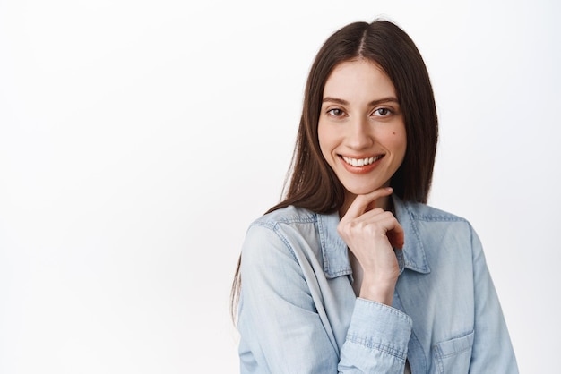 Nahaufnahme einer schönen jungen brünetten Frau, die fasziniert und nachdenklich aussieht. Hmm, das ist ein interessantes Gesicht. Sehen Sie, wie viel nachdenklich vor weißem Hintergrund steht