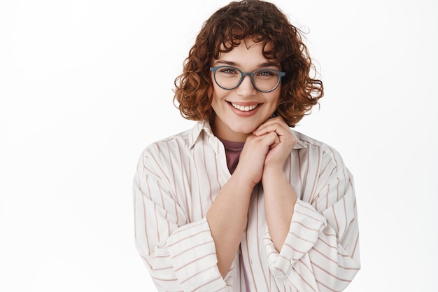 Kostenloses Foto nahaufnahme einer schönen jungen frau mit brille, die schüchtern und zärtlich in die kamera schaut, errötet, flirtet oder etwas nettes anschaut, romantisch vor weißem hintergrund steht