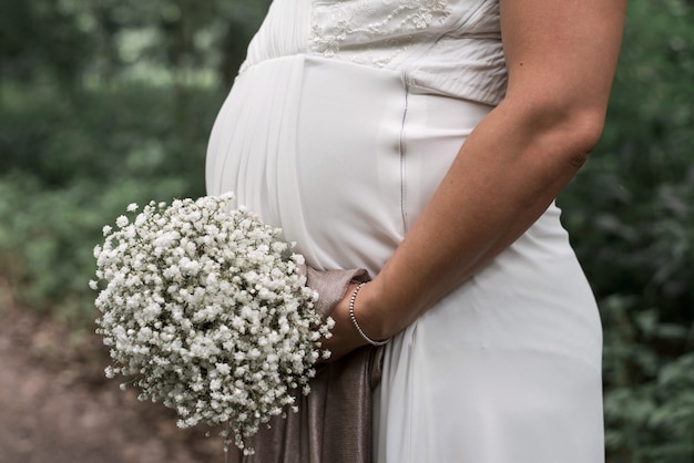 Nahaufnahme einer schwangeren Braut, die an ihrem Hochzeitstag einen weißen Blumenstrauß hält