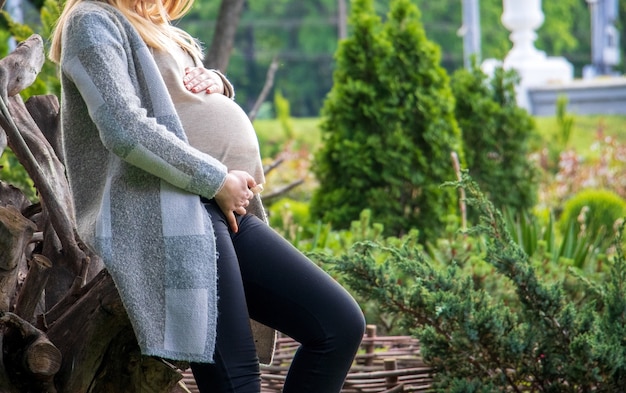 Nahaufnahme einer schwangeren Frau in einer Strickjacke, die ihren Bauch in einem Garten - Mutterschaftskonzept hält