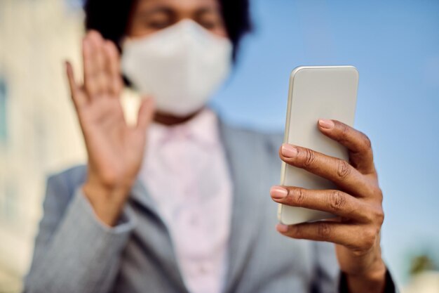 Nahaufnahme einer schwarzen Geschäftsfrau mit Gesichtsmaske mit Smartphone im Freien