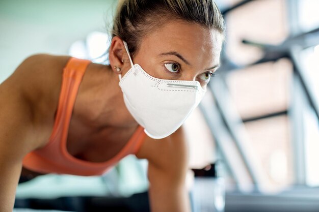 Nahaufnahme einer Sportlerin mit schützender Gesichtsmaske, die im Fitnessstudio trainiert