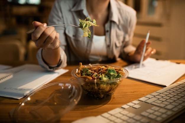 Nahaufnahme einer studentin, die salat isst, während sie nachts zu hause lernt