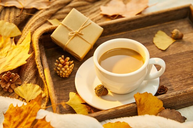 Nahaufnahme einer Tasse Kaffee und Herbstlaub auf Holzuntergrund