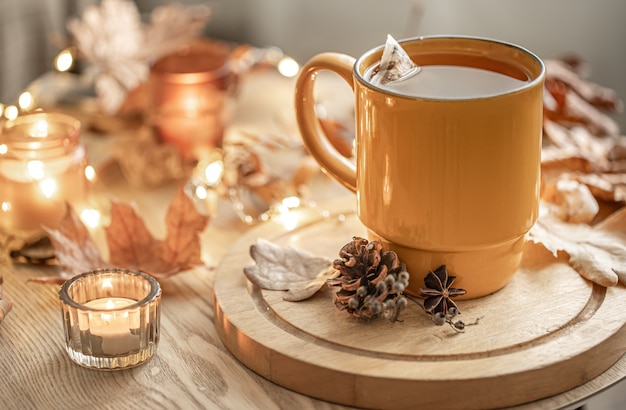 Nahaufnahme einer Tasse Tee unter den Herbstblättern und Kerzen auf einem unscharfen Hintergrund.