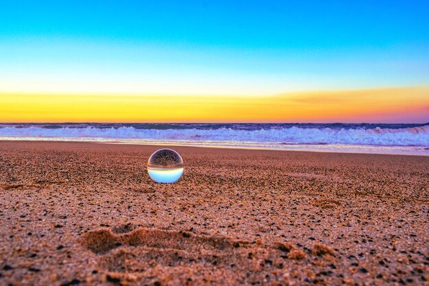 Nahaufnahme einer transparenten Kugel auf dem Sand, der durch das Meer während des Sonnenuntergangs am Abend umgeben ist