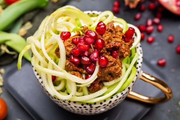 Nahaufnahme einer veganen Mahlzeit mit spiralisierter Zucchini, Tomatensauce und Granatäpfeln in der Tasse