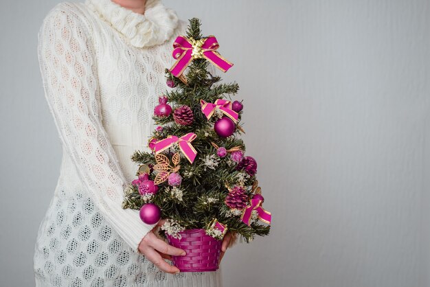Nahaufnahme einer weißen Frau, die einen winzigen Weihnachtsbaum in einem Topf mit lila Verzierungen hält