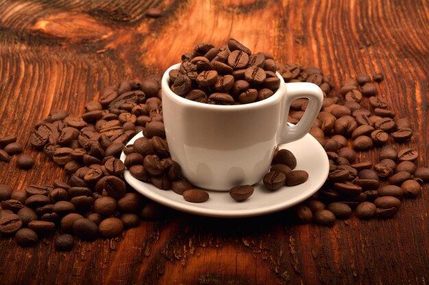 Nahaufnahme einer weißen Tasse voller Kaffeebohnen auf einem Holztisch