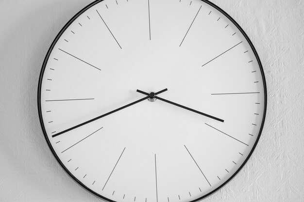 Nahaufnahme einer weißen und schwarzen Uhr auf einer weißen Wand - das Konzept der Zeit