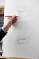 Kostenloses Foto nahaufnahme eines älteren mannes, der künstlerische kunstwerke in der werkstatt des kunstateliers zeichnet. hobby-fähigkeitskurs zeichnen, aktivität für alte menschen im klassenlehrerstudium skizzieren