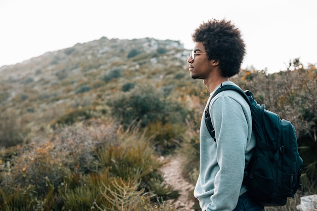 Nahaufnahme eines afrikanischen jungen Mannes mit seinem Rucksack, der vor Berg steht