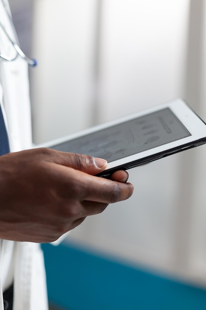 Nahaufnahme eines afroamerikanischen Arztes, der Krankheitsexpertise analysiert, indem er die Patientensymptome während der klinischen Untersuchung mit Tablet überwacht. Spezialist für medizinische Behandlung im Krankenhausbüro