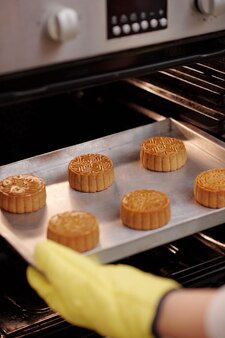 Nahaufnahme eines bäckers, der ein tablett mit gebackenen mondkuchen aus dem ofen nimmt, um für das mittlere herbstfest zu dienen?