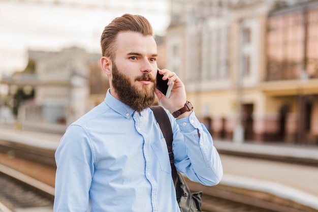 Nahaufnahme eines bärtigen jungen Mannes, der Handy am Bahnhof verwendet