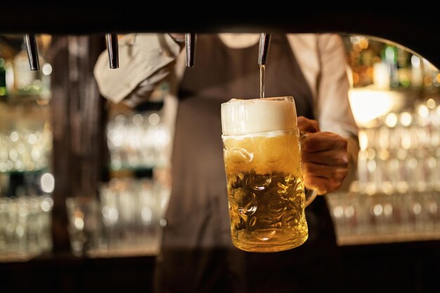 Nahaufnahme eines Baristas, der während der Arbeit in einer Kneipe Bier aus dem Zapfhahn gießt.