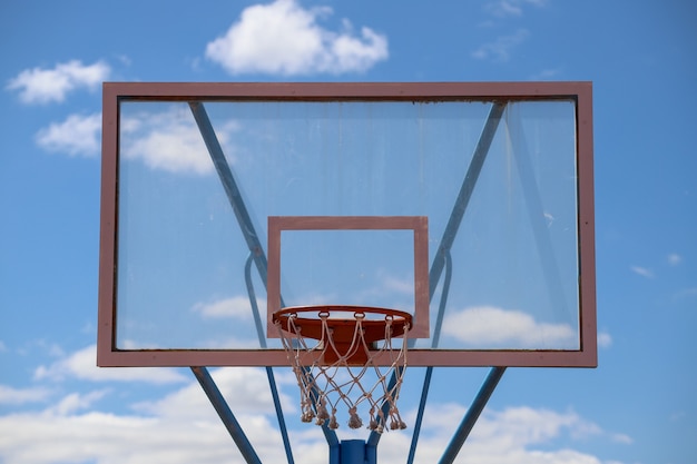 Nahaufnahme eines Basketballkorbs in einem Feld unter Sonnenlicht und blauem Himmel