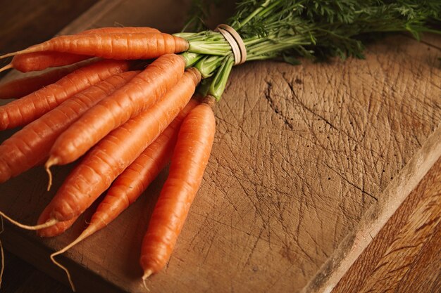 Nahaufnahme eines Bündels frischer reifer Karotten auf einem alten Schneidebrett mit tiefen Schnitten