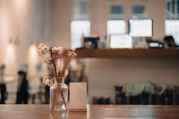 Nahaufnahme eines Café-Holztisches mit einem Glas dekorativer Blumen vor verschwommenem Hintergrund