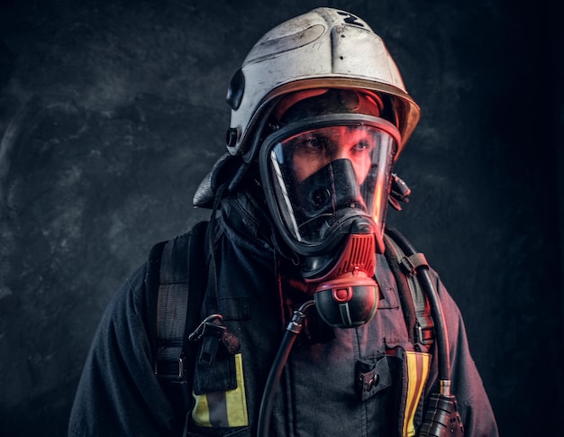 Nahaufnahme eines Feuerwehrmanns mit Schutzhelm und Sauerstoffmaske. Studiofoto gegen eine dunkle strukturierte Wand