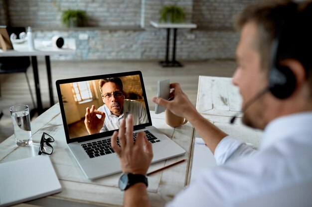 Nahaufnahme eines Geschäftsmannes, der einen Laptop benutzt, während er einen Videoanruf mit einem Kollegen aus dem Büro tätigt