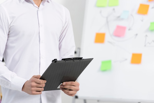 Nahaufnahme eines Geschäftsmannes, der in der Hand das schwarze Klemmbrett hält, das nahe dem Flipchart steht