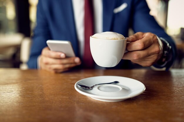 Nahaufnahme eines Geschäftsmannes, der Kaffee trinkt, während er ein Smartphone in einem Café benutzt