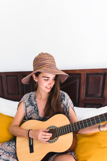 Kostenloses Foto nahaufnahme eines glücklichen jugendsitzens auf dem bett, das gitarre spielt