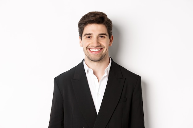 Nahaufnahme eines gutaussehenden jungen Geschäftsmannes im trendigen Anzug lächelnd, stehend vor weißem Hintergrund