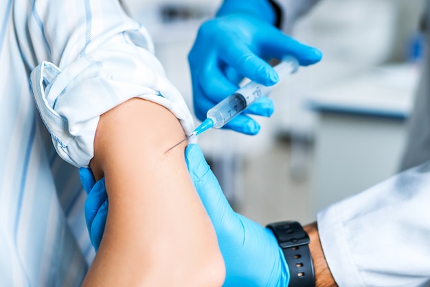 Nahaufnahme eines impfenden mannes, ein arzt in blauen handschuhen steckt eine nadel in seine hand. impfung gegen covid-19
