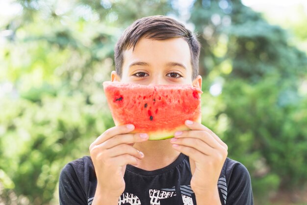 Nahaufnahme eines Jungen, der Wassermelonenscheibe über seinem Mund hält