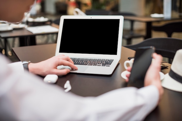 Nahaufnahme eines jungen Geschäftsmannes unter Verwendung des Handys und des Laptops am Arbeitsplatz