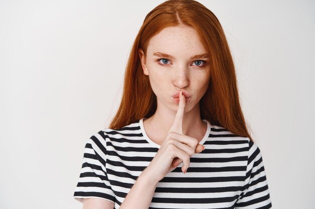 Nahaufnahme eines jungen Ingwermädchens mit ernstem Gesicht, das ein Tabuzeichen zeigt, dich verstummt und ein Geheimnis erzählt