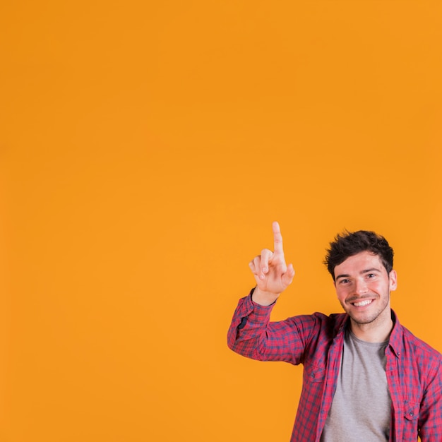 Nahaufnahme eines jungen Mannes, der aufwärts seinen Finger gegen orange Hintergrund zeigt