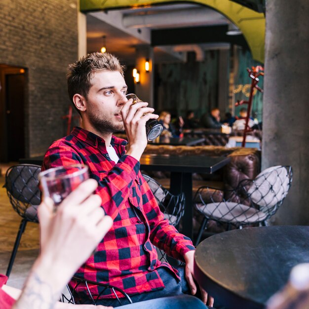 Nahaufnahme eines jungen Mannes, der das Bier mit seinem Freund in der Kneipe trinkt