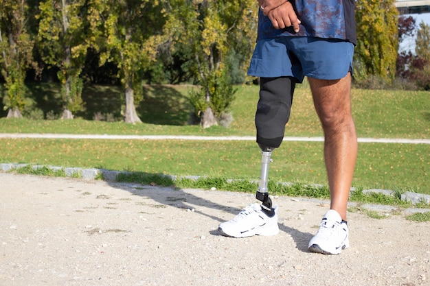 Nahaufnahme eines kaukasischen mannes mit mechanischem bein. sportler in blauen shorts und weißen turnschuhen im park fotografiert. sport, behinderungskonzept