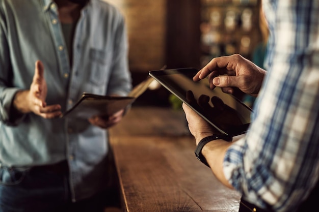 Nahaufnahme eines Kellners, der in einem Café eine Bestellung auf einem digitalen Tablet entgegennimmt