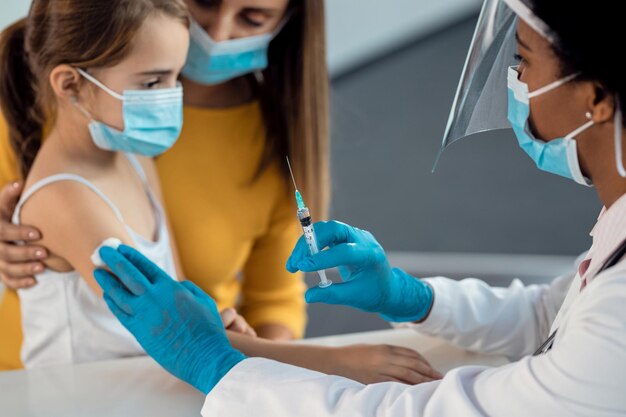 Nahaufnahme eines Kinderarztes, der einem kleinen Mädchen in der Klinik einen Impfstoff verabreicht