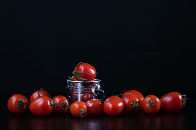 Nahaufnahme eines kleinen Metalleimers mit Kirschtomaten isoliert auf schwarzem Hintergrund