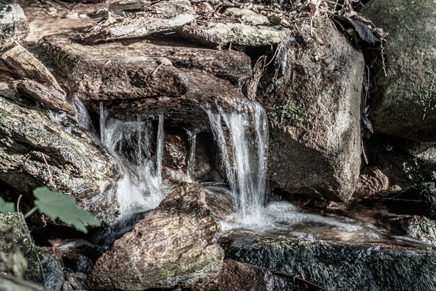 Nahaufnahme eines kleinen Wasserfalls, der tagsüber von Felsen unter dem Sonnenlicht umgeben wird