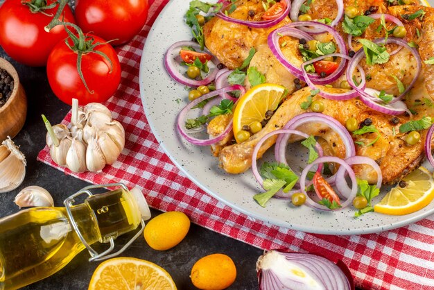 Nahaufnahme eines köstlichen Abendessens gebratenes Hühnergericht mit verschiedenen Gewürzen und Lebensmitteln Tomaten mit Stielen Pfeffer Zwiebeln Knoblauch Ölflasche auf dunklem Hintergrund