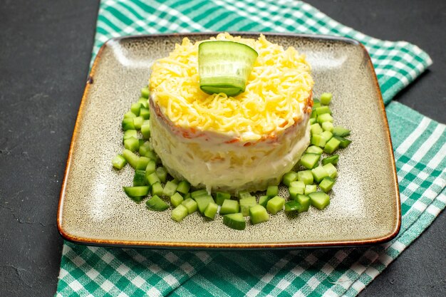 Nahaufnahme eines köstlichen Salats, serviert mit gehackter Gurke auf einem halb gefalteten, grün gestreiften Handtuch auf dunklem Hintergrund
