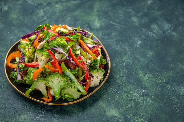 Nahaufnahme eines köstlichen veganen Salats in einem Teller mit verschiedenem frischem Gemüse auf der rechten Seite auf dunklem Hintergrund