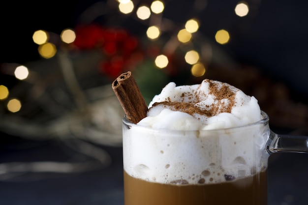 Nahaufnahme eines köstlichen Weihnachtskaffees mit Zimt und Schaum, vor Bokeh-Lichtern