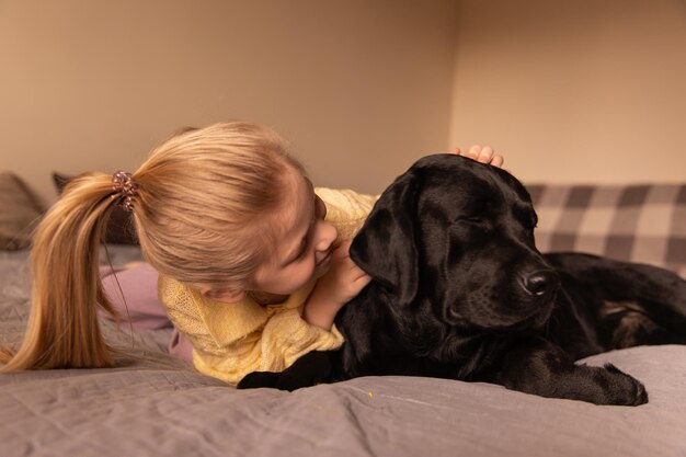 Nahaufnahme eines lächelnden Mädchens, das mit Hund auf dem Bett sitzt