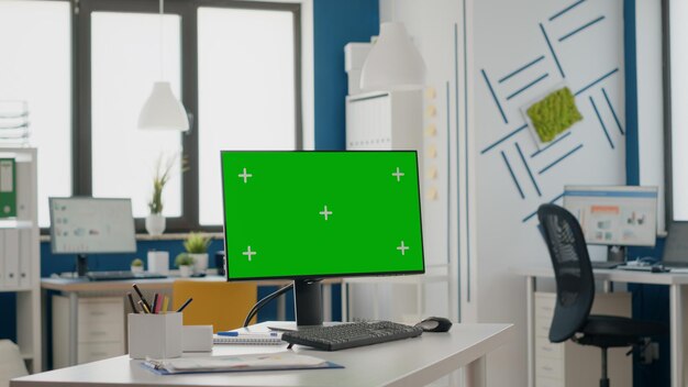 Nahaufnahme eines leeren Schreibtisches mit isoliertem grünem Bildschirm auf dem Monitor. Computer mit Chroma-Key und Mock-up-Vorlage, leerer Hintergrund auf dem Display. Chroma-Key-Kopierraum auf einem digitalen Gerät.