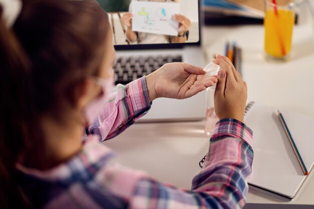 Nahaufnahme eines Mädchens, das Händedesinfektionsmittel benutzt, während es zu Hause lernt