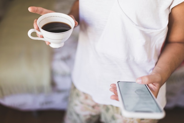 Nahaufnahme eines Mädchens, das Kaffeetasse unter Verwendung des Smartphone hält