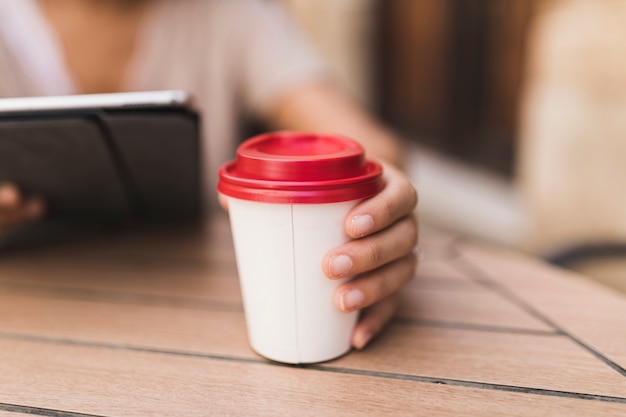 Nahaufnahme eines Mädchens, das Mitnehmerkaffeetasse auf Tabelle hält